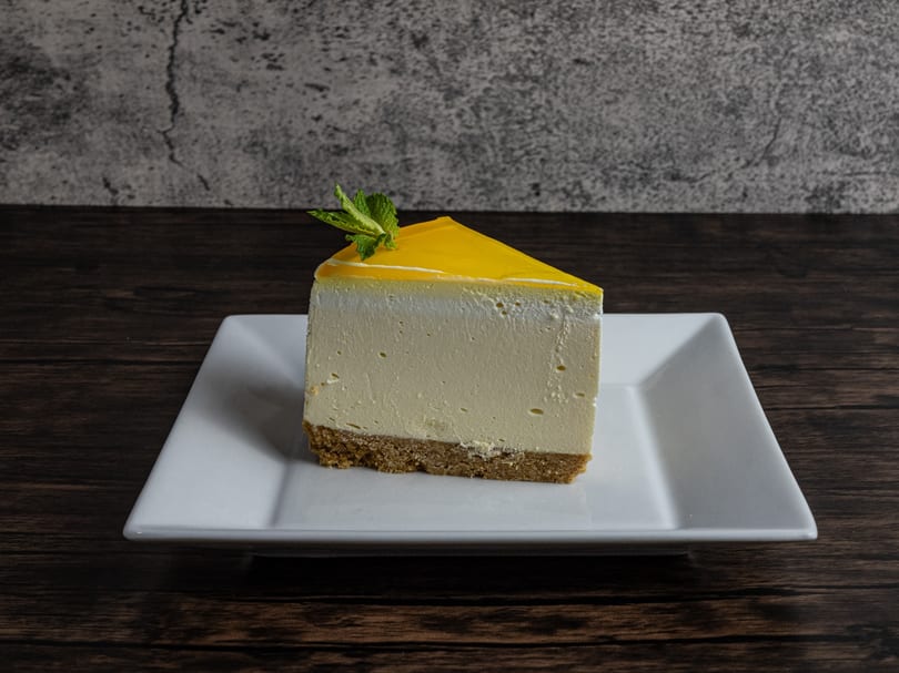 Slice of cheesecake with yellow topping and mint garnish on a white plate.