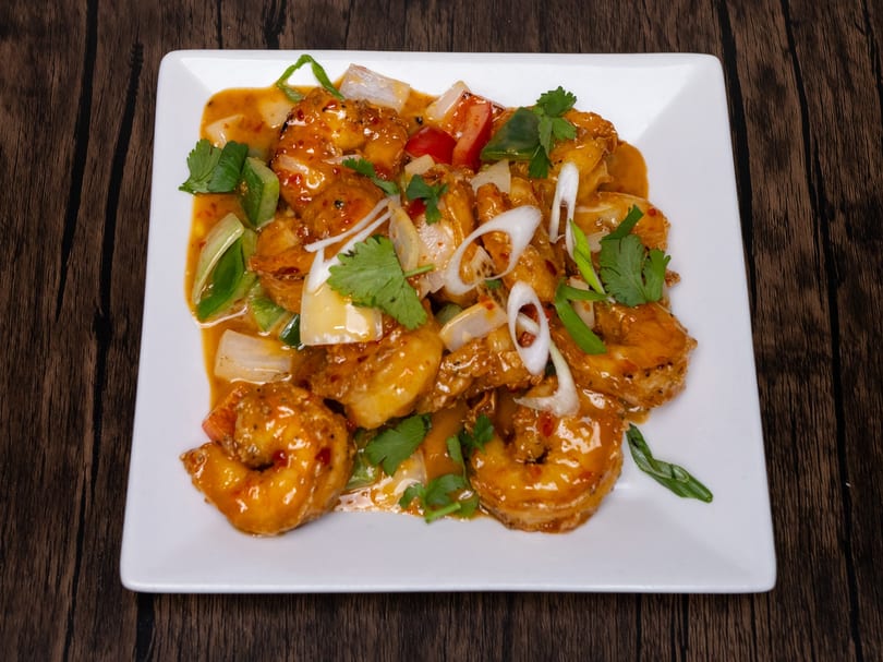 Sweet and sour shrimp with bell peppers, onions, and cilantro on a white rectangular plate.