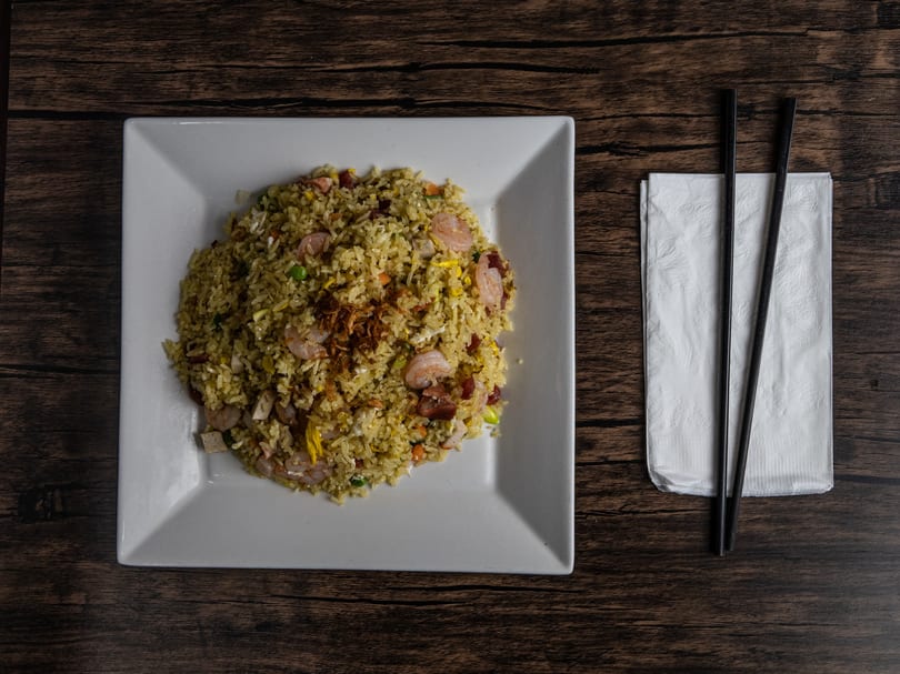 Top-down view of shrimp fried rice on a white square plate with chopsticks and napkin.