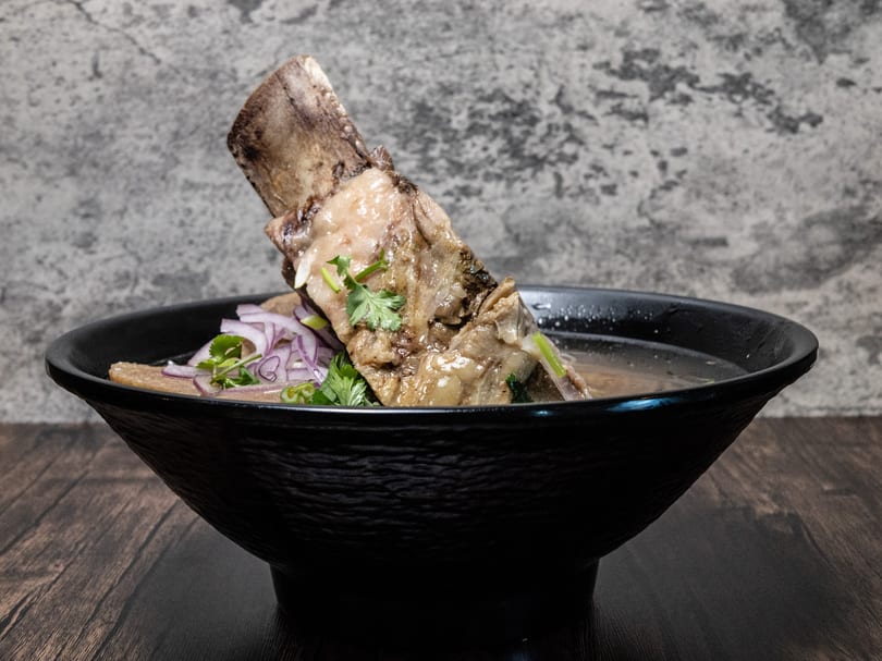 A large bone-in short rib in a bowl of broth, garnished with red onions and cilantro.