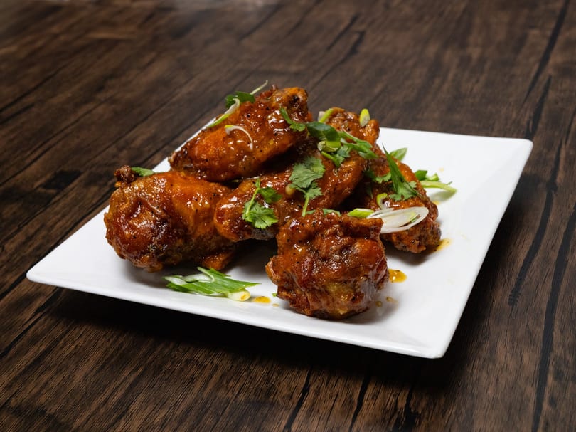 A plate of glistening, saucy chicken wings garnished with fresh cilantro and green onions.